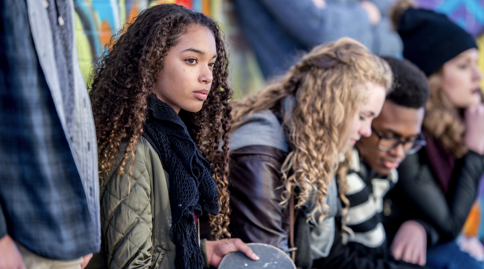 teen with long curly hair looks pensively into the distance while peers are looking at their phones