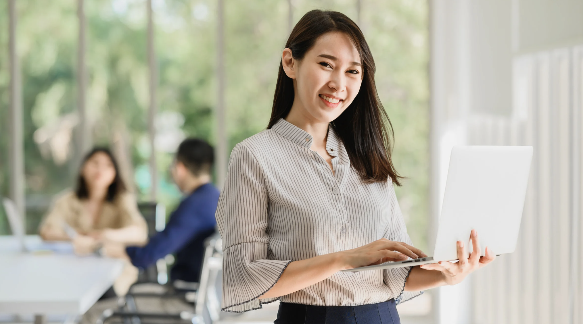 professional east asian woman holding laptop and looking at camera