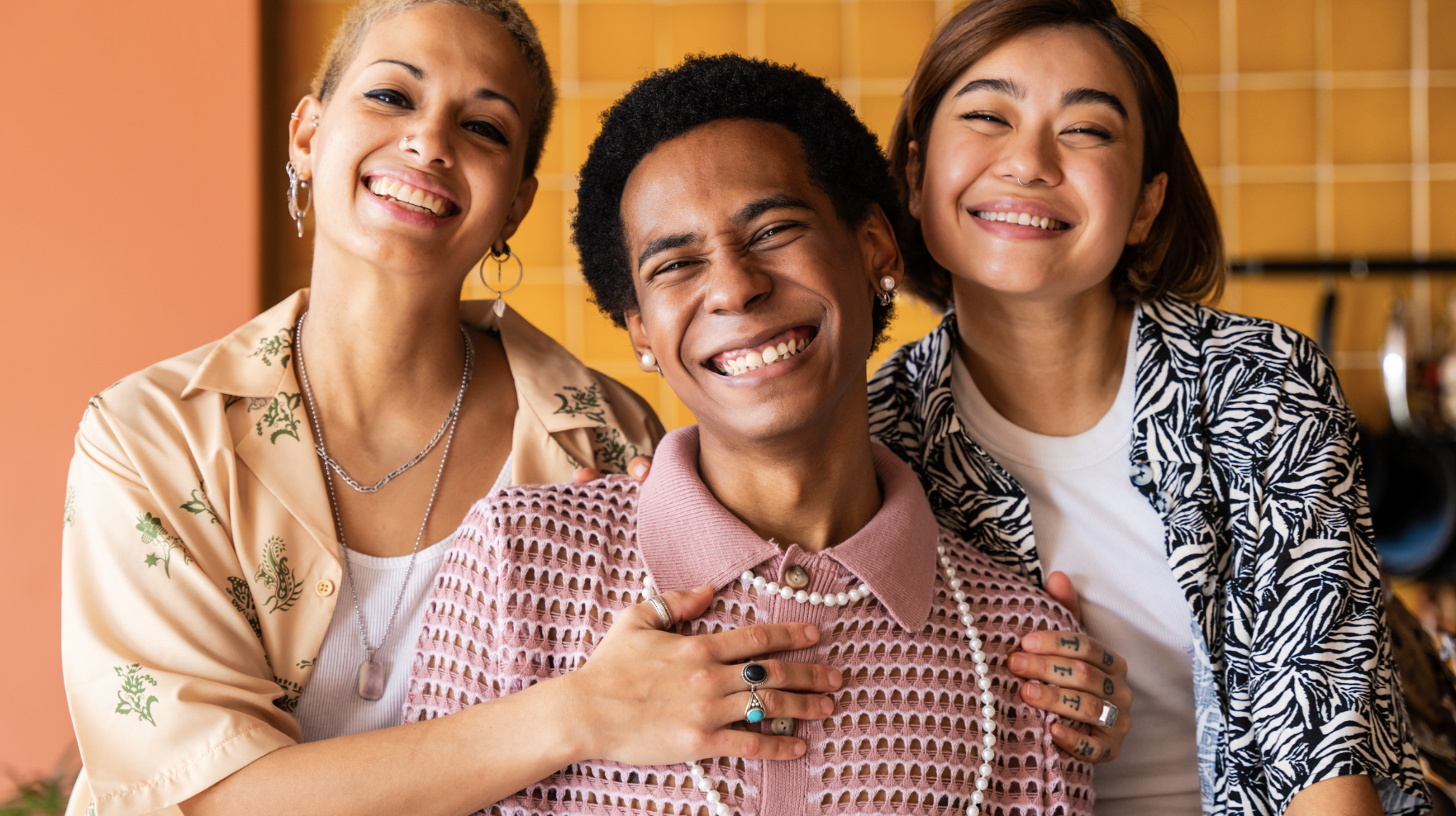 three smiling queer folks against a warm background